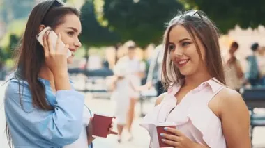 İki çekici genç kadın bir yaz caddesinde konuşuyorlar ve kahve içiyorlar. Kapatın. Uzayı kopyala 4K