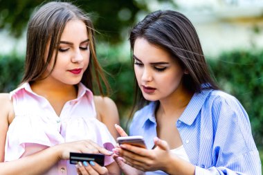 Lovely female friends with smartphones having fun in summer park.