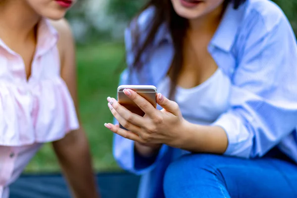 Recortado tiro de encantadoras amigas con teléfono inteligente que se divierten en el parque de verano. Enfoque en smartphone . — Foto de Stock