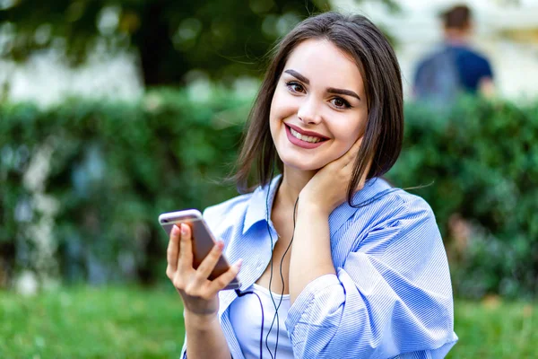 Lovely girl sitting listening to music in park, looking to the camera smiling, peaceful and inspired. — Stock Photo, Image