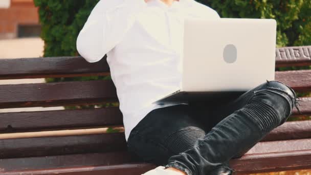 Crop of the unrecognizable man, wearing business style and typing on the laptop computer while sitting outdoors in the park on the bench. Close up. Copy space. 4K. — ストック動画