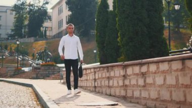 Beyaz gömlekli yakışıklı genç iş adamı sokaklarda yürüyor. Kapatın. Uzayı kopyala 4K.