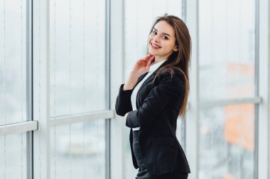 Neşeli kadın pencereden bakıyor, yeni ofisinde hoş duygular ve kendine güvenini ifade ediyor..