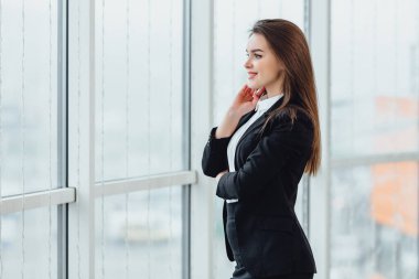 Neşeli kadın pencereden bakıyor, yeni ofisinde hoş duygular ve kendine güvenini ifade ediyor..