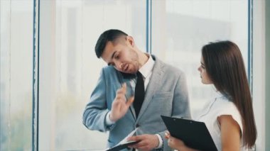 Successful team. Copy space. Boss is busy on the phone. He is seeking for some details in the papers. Blurred white panoramic background. Close up. 4K.