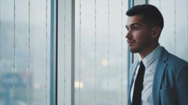 İş adamı pencerenin yanında duruyor. Adam ciddi, izole, beyaz arka planda bulanık görünüyor. Uzayı kopyala 4K.