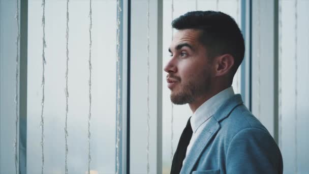 Επιχειρηματίας στέκεται κοντά στο παράθυρο. Ο άνθρωπος κοιτάζει γύρω του, απομονωμένος, σε λευκό θολό φόντο. Αντιγραφή χώρου. 4K. — Αρχείο Βίντεο