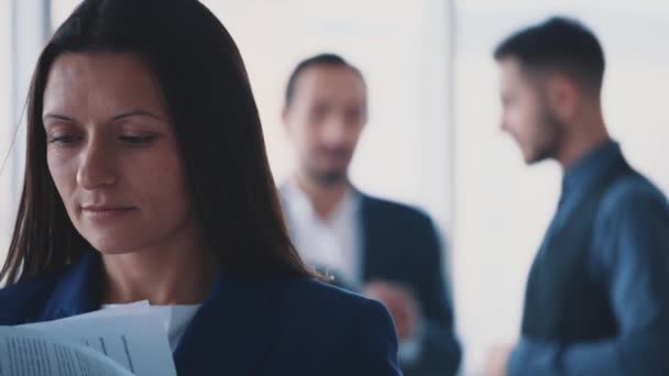 Los trabajadores masculinos de negocios están discutiendo el tema en el fondo borroso luz. La mujer está pasando páginas en la vanguardia. Ella sonríe sinceramente. Copiar espacio. Cultivo. De cerca. 4K . — Vídeo de stock