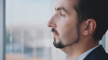 Resmi süitteki iş adamı şehir manzaralı panoramik pencerenin önünde duruyor. Ciddi bir adam. Profil görünümü. Dış profil. Kapatın. Animasyon. 4K.