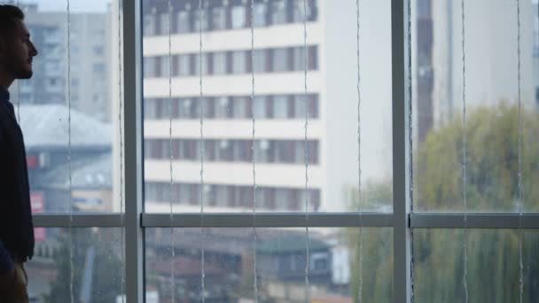 Affärsman i formell svit står framför panoramafönster med utsikt över staden. Närbild. Sakta i backarna. Långsamt. 4k. — Stockvideo