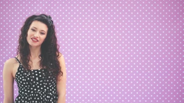 Beautiful young girl with kinky hair and black headband, wearing nice black polka-dots dress is looking at the camera, smiling. — Stock Video