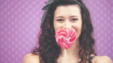 Güzel, genç kıvırcık kız elinde çubuğun üzerinde tatlı kırmızı bir lolipop tutuyor. Bulanık ön cephe.