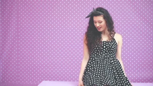 Kinky brunnete κορίτσι με pinup headband κάθεται στο ροζ παγκάκι, απολαμβάνοντας όμορφη polka-dots φόρεμα της. — Αρχείο Βίντεο