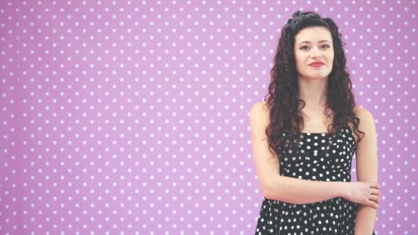 Beautiful young girl with kinky hair and black headband, wearing nice black polka-dots dress is looking at the camera, smiling. — Stock Video