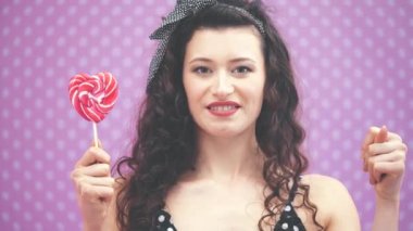 Sevimli genç kıvırcık kız ayakta duruyor, bir elinde tatlı kırmızı lolipopu tutuyor, diğer elinde ise hiçbir şey yok..