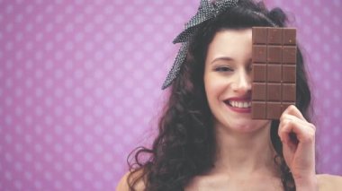 Kıvırcık siyah saçlı, saç bantlı, puantiyeli güzel bir bayan bir çikolata çubuğunun arkasına gözünü gizliyor..