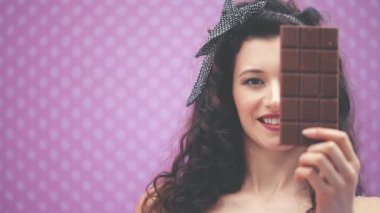 Kıvırcık siyah saçlı, saç bantlı, puantiyeli güzel bir bayan bir çikolata çubuğunun arkasına gözünü gizliyor..