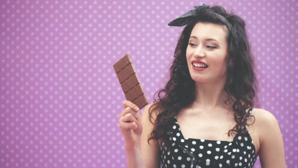 Όμορφη νεαρή σγουρή κοπέλα προσπαθεί να δαγκώσει μια σοκολάτα, αλλά είναι πάρα πολύ δύσκολο. — Αρχείο Βίντεο