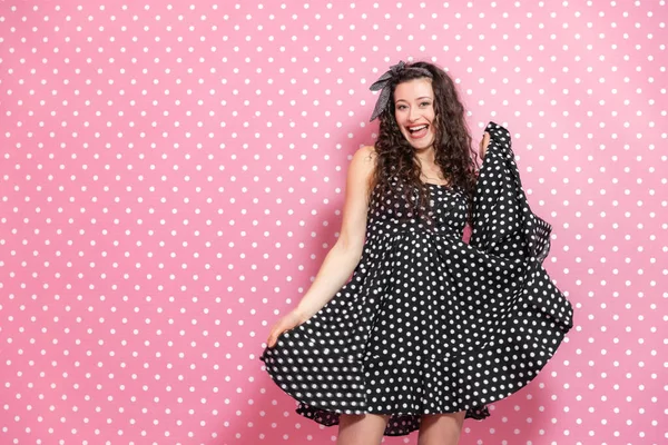 Fashionable girl with wide shining smile is posing, raising one side of her dress. — Stock Photo, Image