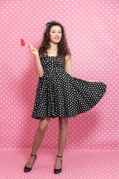 Słodka dziewczyna pozowała, podnosząc jedną stronę sukienki i trzymając lizaka na patyku w dłoni. — Zdjęcie stockowe