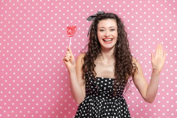 Une jeune femme souriante tient une sucette rouge sur le bâton et salue la caméra . — Photo