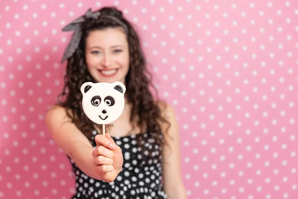 Konzentrieren Sie sich auf den panda-artigen Lutscher am Stock. Schöne verschwommene Mädchen lächeln, blicken in die Kamera und strecken die Süßigkeiten aus. — Stockfoto