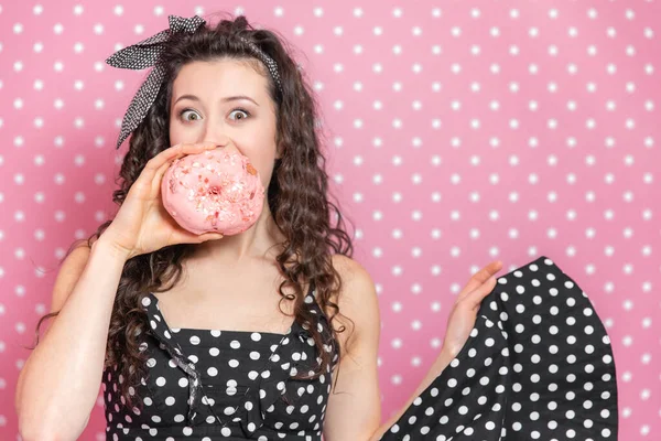 Zauberhaftes Mädchen hält einen Donut vor den Mund, zieht die Augenbrauen hoch und hält die Augen weit offen. — Stockfoto