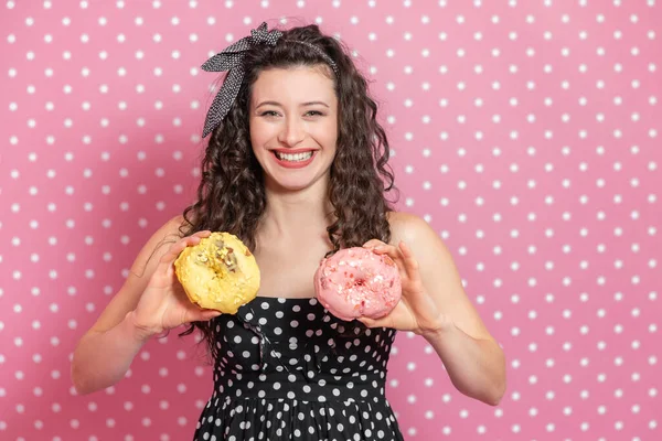 Hübsches Mädchen mit verworrenem Haar und Pin-up-Schleife spielt herum und hält zwei große Donuts auf ihrer Brust und lacht extrem. — Stockfoto