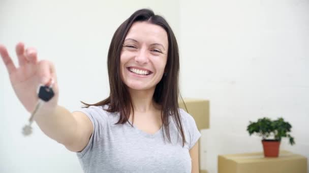 Toothy vrouwelijke appartement eigenaar of huurder tonen sleutels van de camera, terwijl haar man dragen dozen op de wazige achtergrond. — Stockvideo