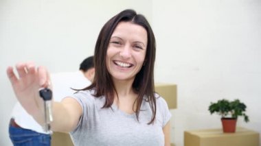 Dişi dişli kadın daire sahibi ya da kiracı kameranın anahtarlarını gösterirken kocası arka planda bulanık kutular taşıyor..