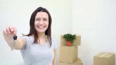 Dişi dişli kadın daire sahibi ya da kiracı kameranın anahtarlarını gösterirken kocası arka planda bulanık kutular taşıyor..