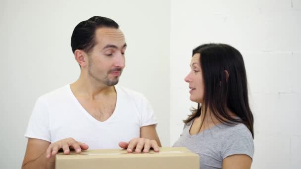 Nadšený mladý pár stojící opřený o lepenkovou krabici v novém bytě, diskutující o uspořádání domu. — Stock video