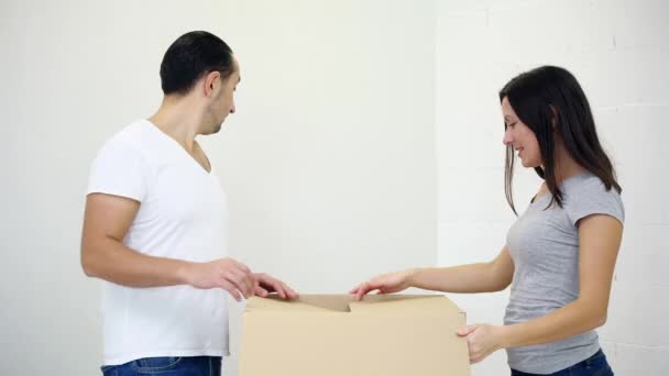 Ευτυχισμένο ενθουσιασμένο ζευγάρι ανοιχτό κουτί από χαρτόνι μαζί στο σπίτι και γέρνει μέσα στο κουτί για να δείτε και να ξεχωρίσετε τι είναι μέσα. — Αρχείο Βίντεο