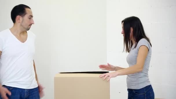 Happy excited couple open cardboard box together at home and leaning inside the box to see and pick out a key to new house. — Stock Video
