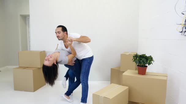 Compradores de casas por primera vez pareja bailando riendo y divirtiéndose juntos en la sala de estar con pilas de cajas . — Vídeos de Stock