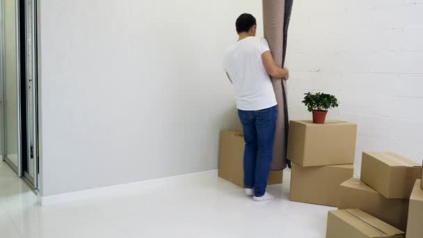Νεαρό ζευγάρι απλώνει ένα χαλί σε ένα νέο διαμέρισμα γεμάτο χαρτοκιβώτια. — Αρχείο Βίντεο