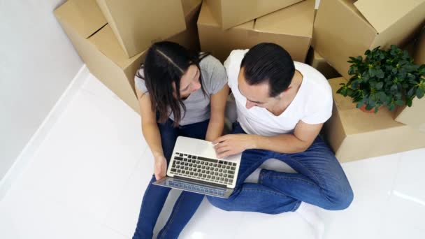 Paar zitten op de vloer van hun nieuwe flat en het maken van online winkelen op laptop, het kiezen van meubels en decorelementen. — Stockvideo