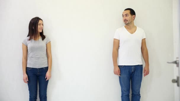 Attraktive Männer und Frauen stehen auf verschiedenen Seiten des weißen Hintergrunds, zeigen auf den Kopierraum zwischen ihnen und lächeln.. — Stockvideo