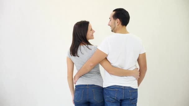 Charmant couple se tient avec le dos à la caméra et regarde le fond de l'écran blanc, pointant vers quelque chose . — Video