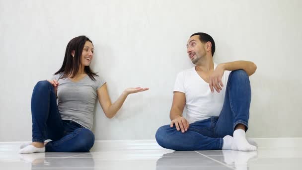 Brunette homme et femme assis sur fond de mur blanc et levant les mains, montrant la croissance et le succès . — Video