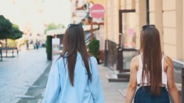 İki güzel kız alışveriş yaptıktan sonra alışverişleriyle sokakta yürürken eğleniyor. Arkadan bak. Uzayı kopyala 4K.