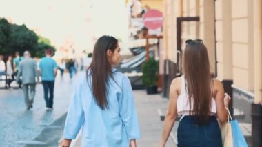 İki güzel kız alışveriş yaptıktan sonra alışverişleriyle sokakta yürürken eğleniyor. Arkadan bak. Uzayı kopyala 4K.