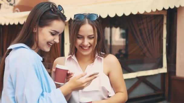 Deux jolies jeunes femmes parlent dans une rue d'été et boivent du café. Ferme là. Espace de copie. 4K — Video