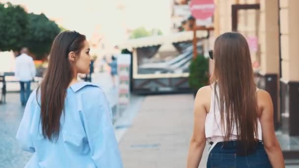 Duas meninas bonitas se divertir andando pela rua com suas compras depois de fazer compras. Fecha. Vista traseira. Espaço para cópia. 4K . — Vídeo de Stock