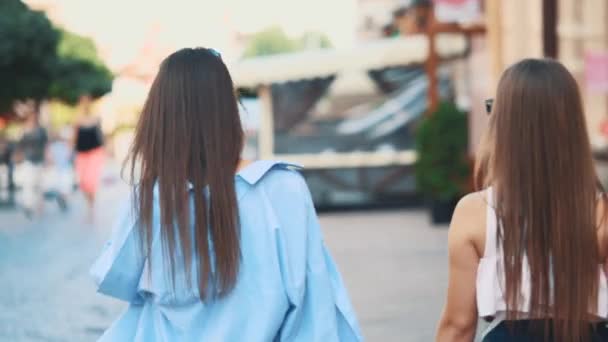 Duas meninas bonitas se divertir andando pela rua com suas compras depois de fazer compras. Fecha. Vista traseira. Espaço para cópia. 4K . — Vídeo de Stock