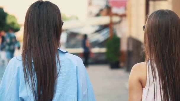 Dos hermosas chicas se divierten caminando por la calle con sus compras después de ir de compras. Vista trasera. Copiar espacio. 4K . — Vídeo de stock