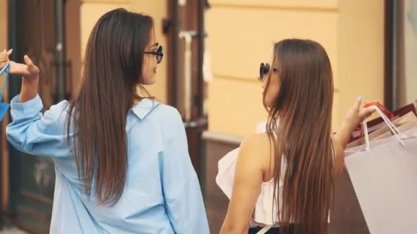 Deux belles filles s'amusent à tenir des achats après les achats. Vue de derrière. Espace de copie. 4K . — Video