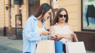 İki çekici genç kadın alışveriş hakkında konuşuyor. Birbirlerine alışverişleri gösteriyorlar. Kapatın. Uzayı kopyala 4K