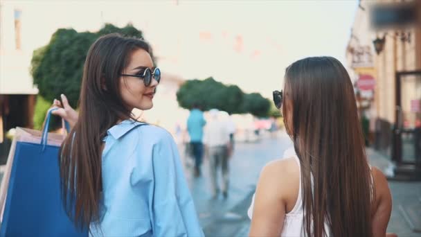 Duas meninas bonitas se divertir segurando compras depois de fazer compras. Vista traseira. Espaço para cópia. 4K . — Vídeo de Stock