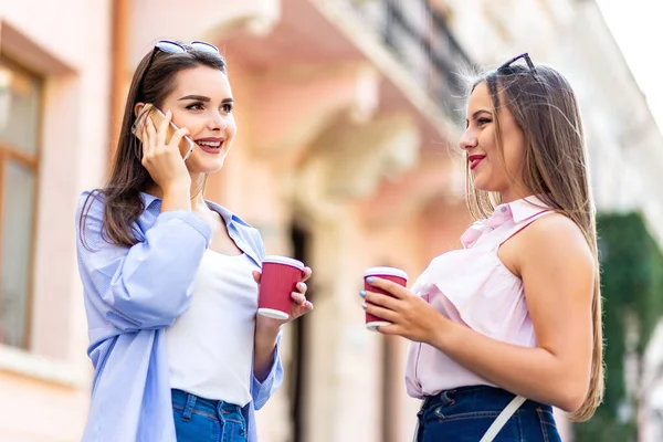Outdoors fashion portrait of two young beautiful women friends drinking coffee and interactiong after shopping. — Φωτογραφία Αρχείου